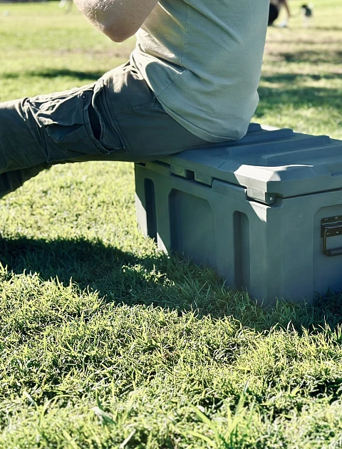 Someone sitting on a closed poly cargo box outdoors, showing how much weight it can take