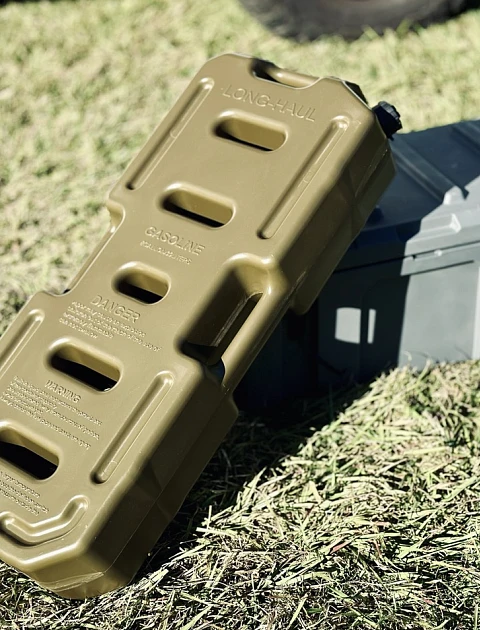 A heavy-duty fuel jerry can standing in the grass next to a small ammo storage box