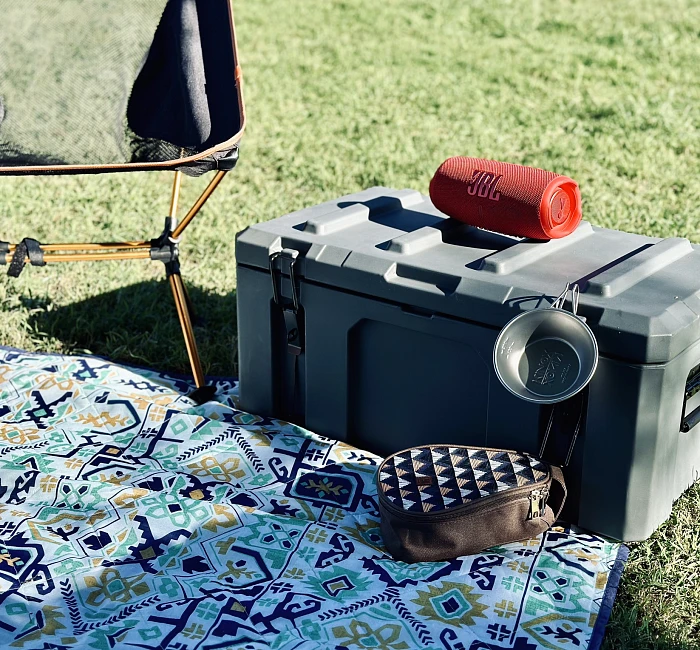 A heavy-duty poly cargo box set up at a campsite with a camp chair, speaker and cookware on top